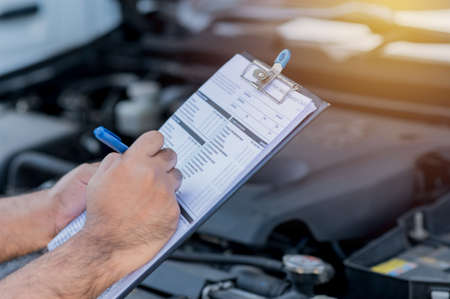 A car maintenance worker is checking a list of the car engine for a workshop customer.の写真素材