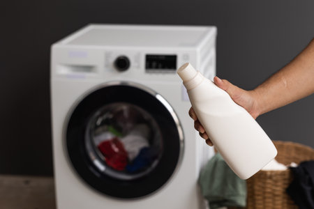 A man with a bottle of laundry detergent About to pour the detergent into the washing machine