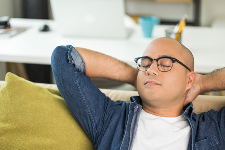 Young asian man Sit and relax in the living room on the sofa. He rested from work raise hands on...
