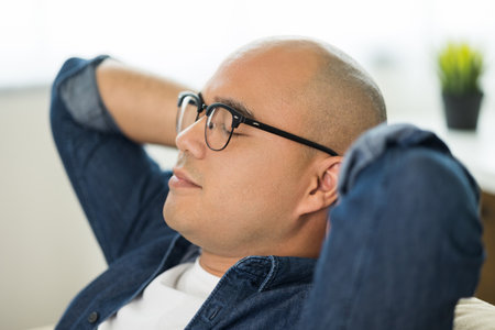 Young asian man Sit and relax in the living room on the sofa. He rested from work raise hands on head and smile.の写真素材
