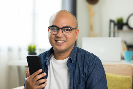 Young asian man Sit and relax in the living room on the sofa.He using texting smartphone and smile.