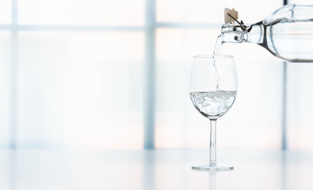 A transparent glass of water is placed on the table and a water bottle is poured into the glass in...