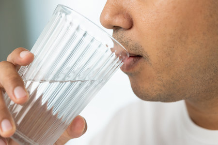 A young man drinking clean water from a clear glass For good health, drink water regularly. He was...