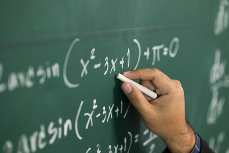 Education background concept. Close up male hand writing mathematical formula on chalkboard.