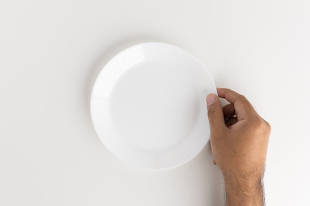 A man's hand is putting a white empty plate on the tableの写真素材