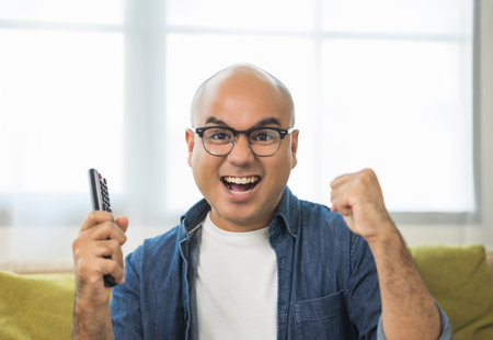 Young asian man watching television using remote to change the program. He very enjoy and excited....