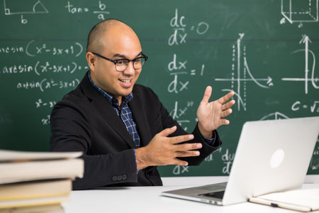 Indian young teacher man sitting teaching online video conference live stream by laptop. Asian teacher teaching mathematics class webinar online for students learning.の写真素材
