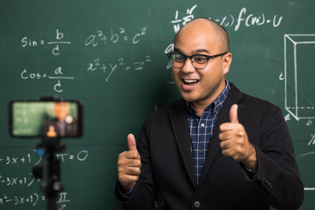 Indian young teacher man teaching online video conference live stream by smartphone. Asian teacher teaching mathematics class webinar online for students learning.の写真素材