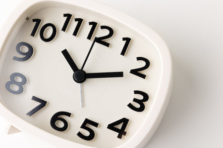 Small white alarm clock, black numbers, set the time for 10.10 o'clock, placed on a white table.