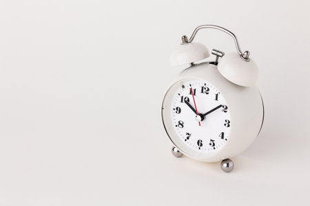 Small white alarm clock, black numbers, set the time for 10.10 o'clock, placed on a white table.の写真素材