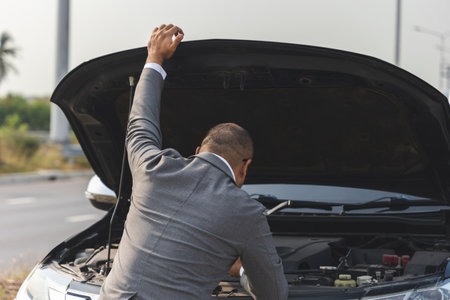 Young asian business has broken down car. He open hood and check the engine. He feeling upset and stressed. Car broken on the side of the roadの写真素材