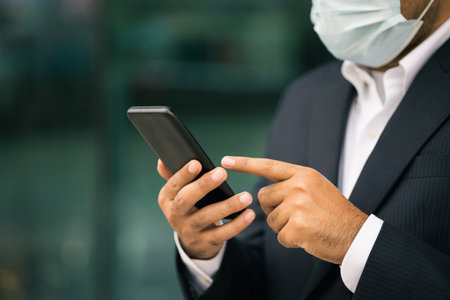 Young businessman wearing protection mask using smartphone in downtown urban city. Asian man in suit walking in the city.の写真素材