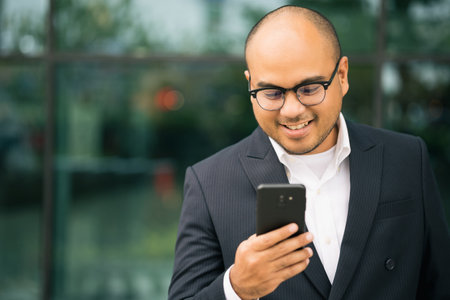 Young indian businessman using smartphone standing in front of building office. Asian businessman using in suit using on cellphone.の写真素材