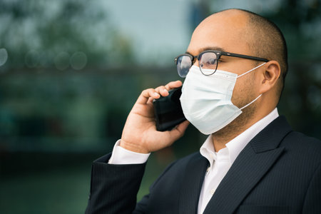 Young businessman wearing protection mask using smartphone in downtown urban city. Asian man in suit walking in the city.の写真素材