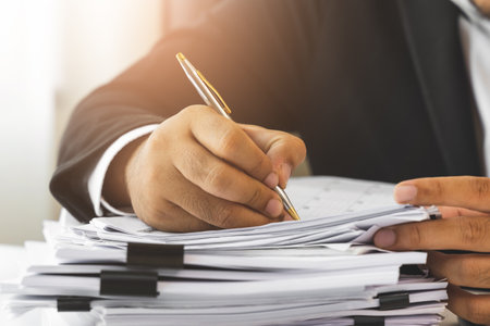 A young businessman in a suit is signing documents for a variety of tasks in the office. Many...