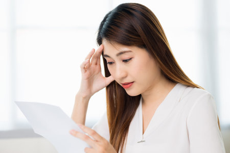 Young asian business woman hand touching head looking at paper work or bills she's feeling depressed stress headache be tired from working with laptop a long time she symptom office syndrome.の写真素材