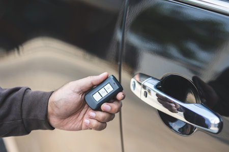 Close up male hand holding car key. Man unlock car door by remote key push button near car door.