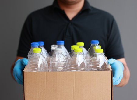 A young man wearing rubber gloves arranged plastic bottles into a carton. He assumes plastic bottles will sort of trash before throwing them into the bin.の写真素材