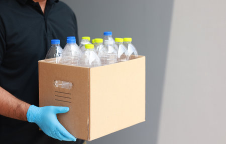 A young man wearing rubber gloves arranged plastic bottles into a carton. He assumes plastic bottles will sort of trash before throwing them into the bin.の写真素材