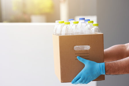 A young man wearing rubber gloves arranged plastic bottles into a carton. He assumes plastic bottles will sort of trash before throwing them into the bin.の写真素材