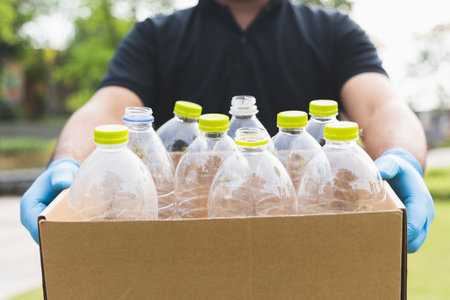 A young man wearing rubber gloves arranged plastic bottles into a carton. He assumes plastic bottles...