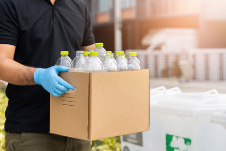 A young man wearing rubber gloves arranged plastic bottles into a carton. He assumes plastic bottles will sort of trash before throwing them into the bin.の写真素材