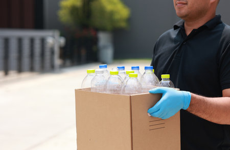 A young man wearing rubber gloves arranged plastic bottles into a carton. He assumes plastic bottles will sort of trash before throwing them into the bin.の写真素材