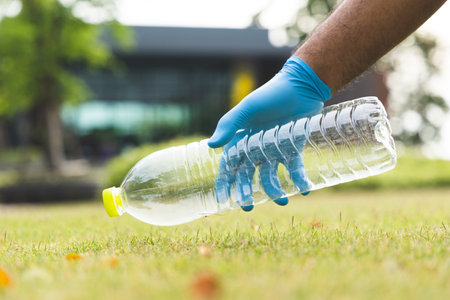 Young male volunteers Volunteer to collect garbage Plastic bottles to the city He wears rubber gloves, collects plastic bottles from the lawn and takes them to separate litter before throwing away.の写真素材