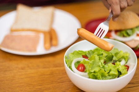 A young man eating breakfast. Breakfast set includes bread, bacon, salad and sausage.の写真素材
