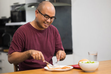 A young man eating breakfast. Breakfast set includes bread, bacon, salad and sausage.