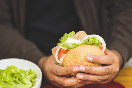 Man eating breakfast Hamburger buns stuffed with vegetables and meat and tomatoes Healthy breakfast It has good carbohydrates and vitamins. Fast food to eat in the morning before going to workの写真素材