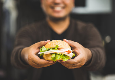 Man eating breakfast Hamburger buns stuffed with vegetables and meat and tomatoes Healthy breakfast It has good carbohydrates and vitamins. Fast food to eat in the morning before going to workの写真素材