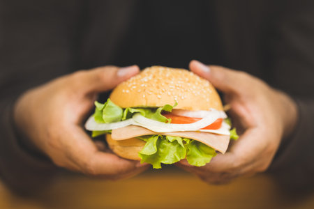 Man eating breakfast Hamburger buns stuffed with vegetables and meat and tomatoes Healthy breakfast It has good carbohydrates and vitamins. Fast food to eat in the morning before going to workの写真素材