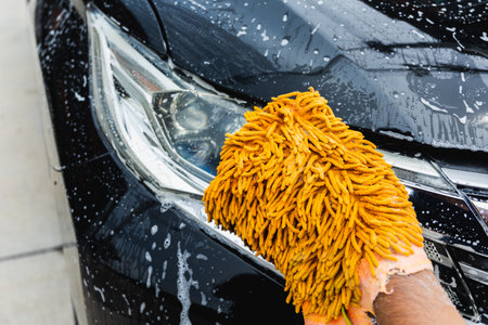 The young man washed his car with foamy cleansing foam. He was wearing gloves for washing the car....
