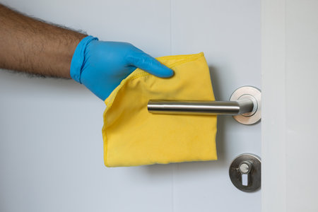The young man cleaned the door locks by spraying cleaning agents to kill germs and viruses for hygiene. He put on rubber gloves and wipes.の写真素材