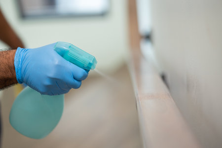 A young man cleans the stair handrail by spraying a cleaner viruses for good hygiene. He put on...
