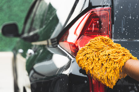 The young man washed his car with foamy cleaning foam. He was wearing gloves for washing the car. He wiped the car's tail lights and body.の写真素材