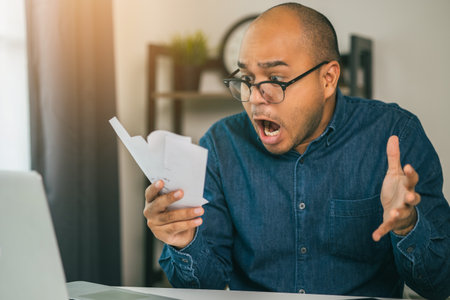 A young Asian man is stressed because he looks at many expense bills and he has no money to pay...