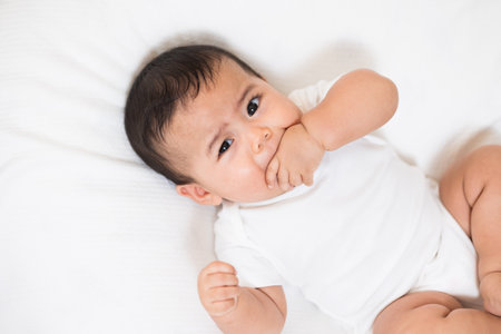 A cute baby in a white dress is crying. Stay with parents in the house