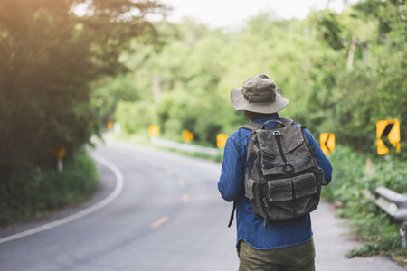Young handsome man with a backpack is walking alone the road. Man is looking forward to an interesting travelling.の写真素材