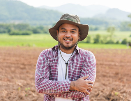Happy farmer with hat standing and smiling in plantation field at sunset.の写真素材