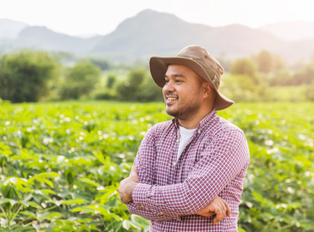 Happy farmer with hat standing and smiling in plantation field at sunset.