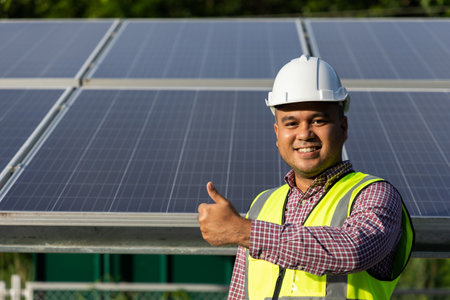 Young asian electrical engineer standing in front of Solar cell panels farm. He showing thumbs up. Solar generator power concept.の写真素材
