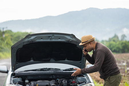 Asian man has  broken down car on the road he talking on phone to call someone to help or mechanics...