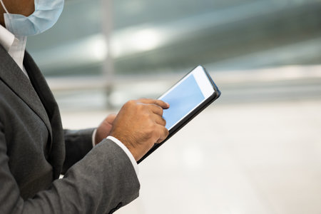 Businessman in airport terminal working with tablet . He wearing mask protection corona virus. He check in and waiting in passenger building.の写真素材