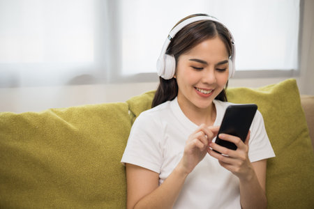 Relaxing time on sofa. Beautiful young asian woman sitting on sofa she choose music from smartphone...