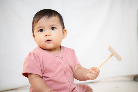 An Asian girl about 1 year old. Playing wooden toy in the living room in the house. A cute baby wearing a pink dress Stay with parents in the houseの写真素材