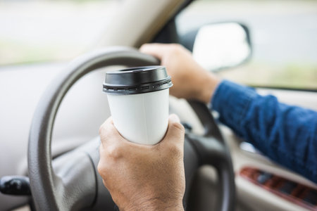 Young man drinking a cup of hot coffee while driving car to travel. Hands holding steering wheel.