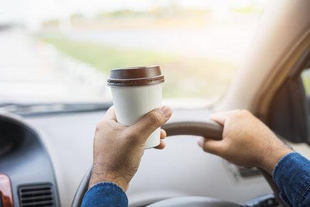 Young man drinking a cup of hot coffee while driving car to travel. Hands holding steering wheel.
