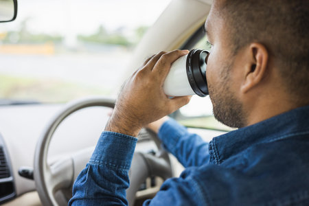 Young man drinking a cup of hot coffee while driving car to travel. Hands holding steering wheel.